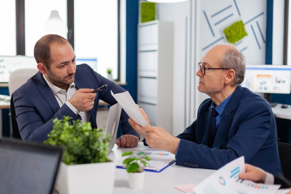 senior-entrepreneur-discussing-with-coworker-holding-documents-conference-briefing-businessman-discussing-ideas-with-colleagues-about-financial-strategy-new-start-up-company_482257-5074